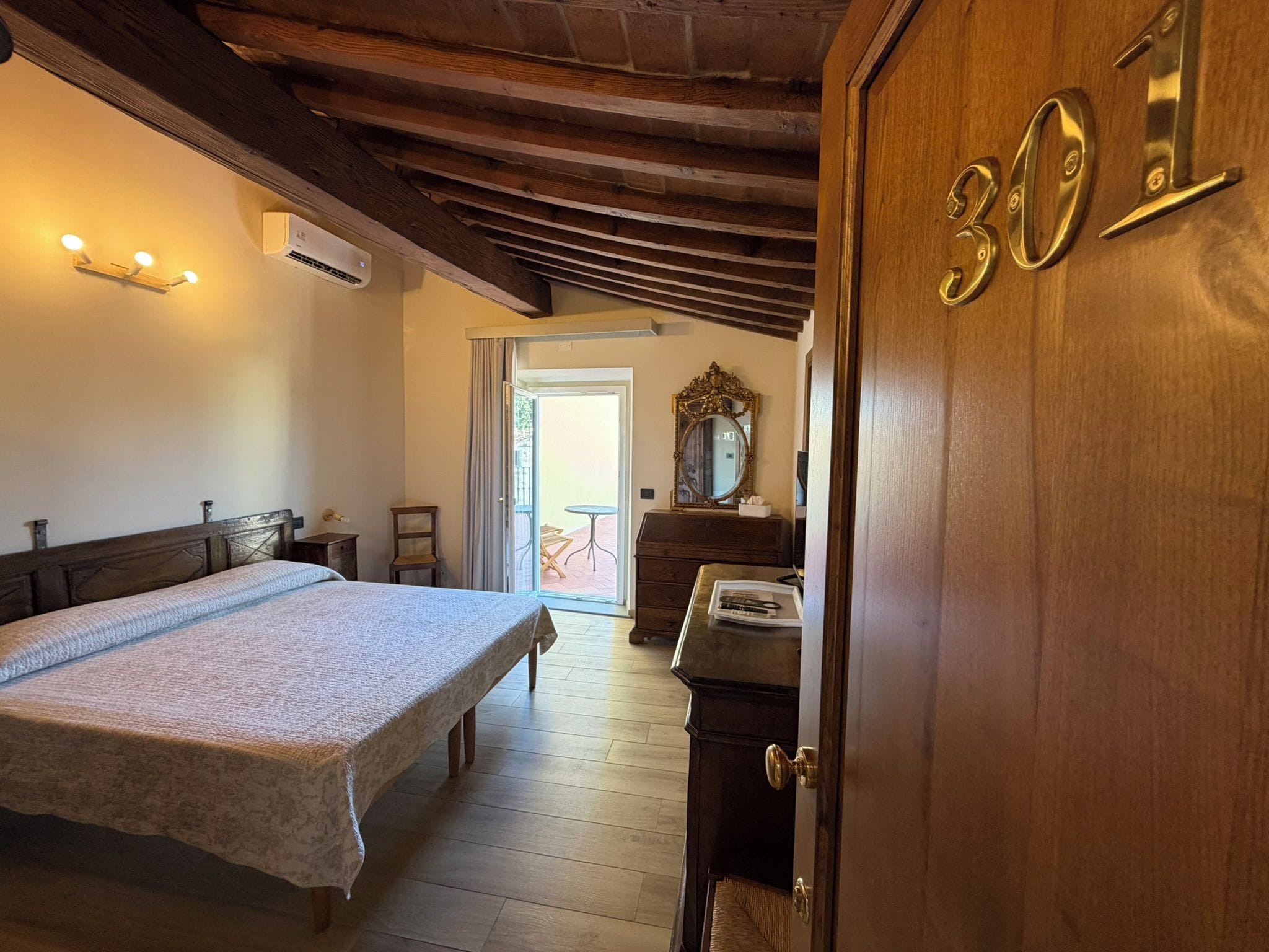 Un dormitorio con cama, una puerta de madera con un número, un espejo y una ventana.