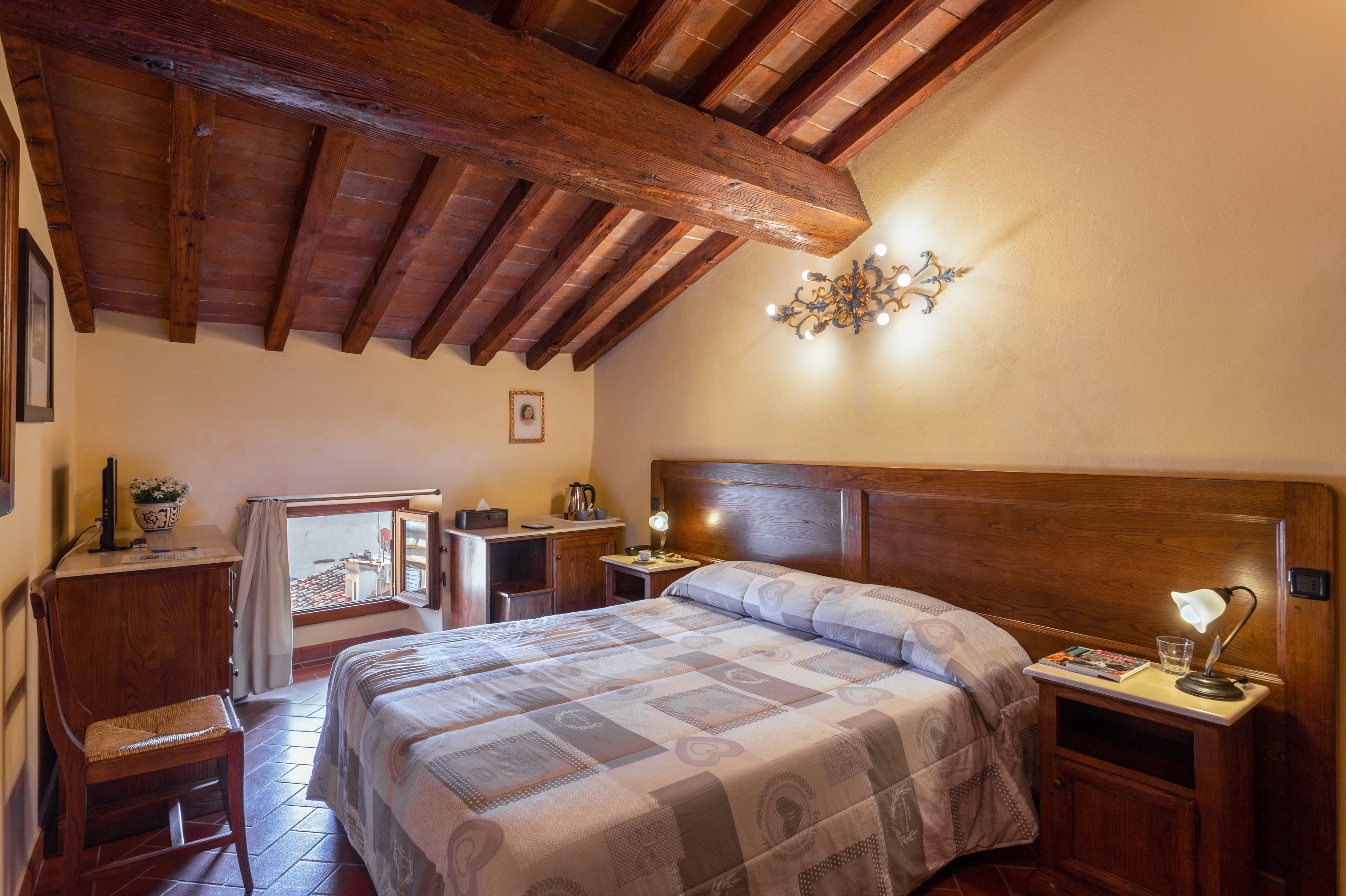 Un dormitorio con techo de madera, una cama con colcha, un escritorio con silla y una mesita de noche con lámpara.