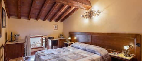 Un dormitorio con techo de madera, una cama con colcha, un escritorio con silla y una mesita de noche con lámpara.