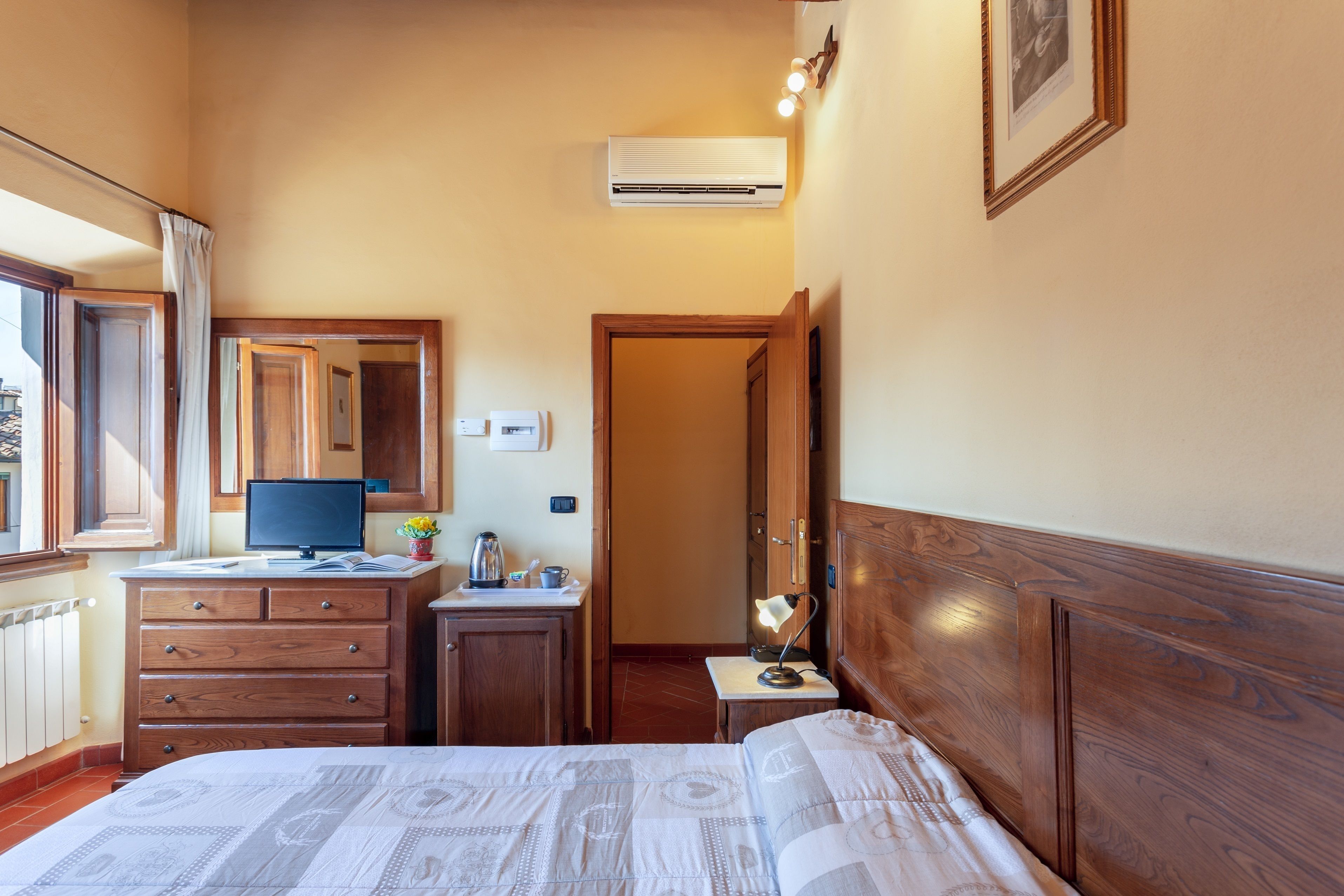 Une chambre d’hôtel comprenant un lit, un bureau avec un ordinateur, une chaise, une petite table avec une lampe et un appareil de climatisation.