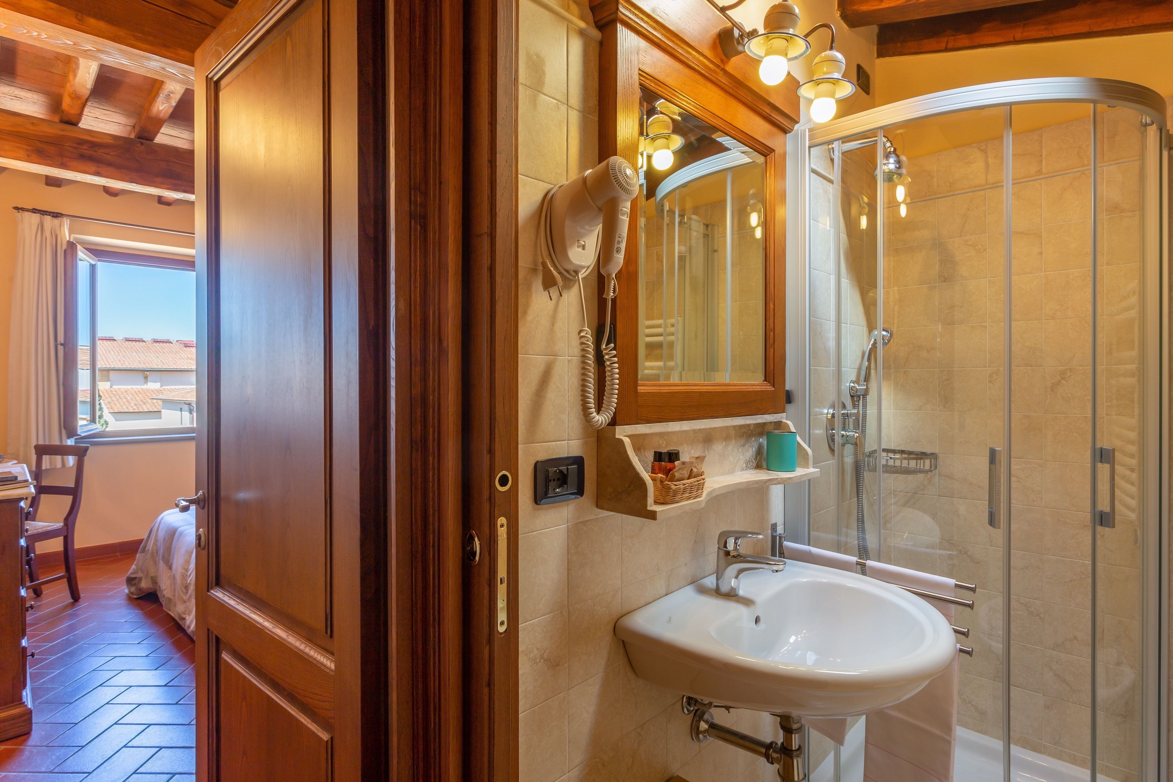 A bathroom with a glass shower, a white sink, and a hairdryer mounted on the wall.