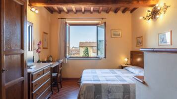 Ein Schlafzimmer mit einem Bett, einem Schreibtisch, einem Stuhl, einer Kommode und einem Fenster mit Blick auf Gebäude.