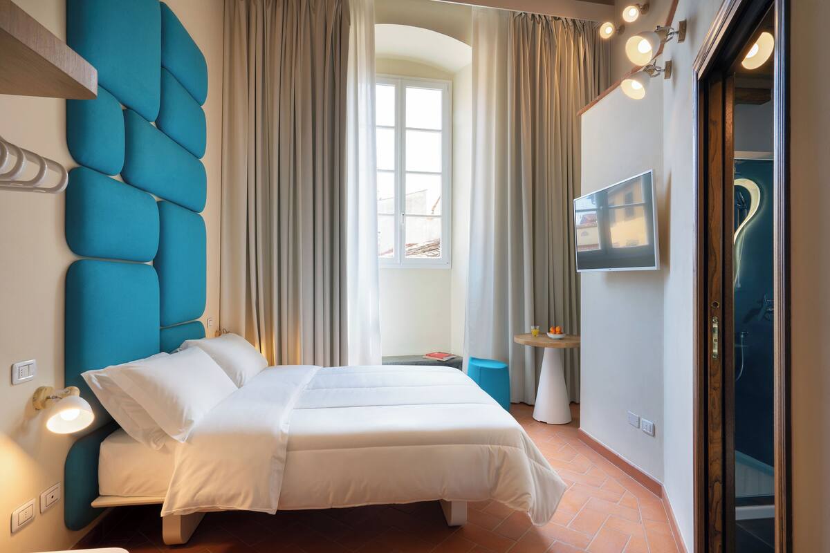 Een hotelkamer met een bed, een televisie, een badkamer met douche en een raam met gordijnen.
