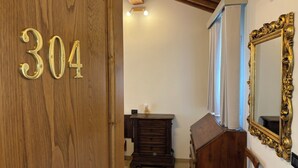 Una puerta de madera con el número 304, un aparador de madera oscura, un espejo con un marco dorado ornamentado y un techo con vigas de madera a la vista.