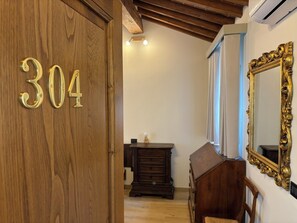 A wooden door with the number 304, a dark wooden dresser, a mirror with an ornate gold frame, and a ceiling with exposed wooden beams.