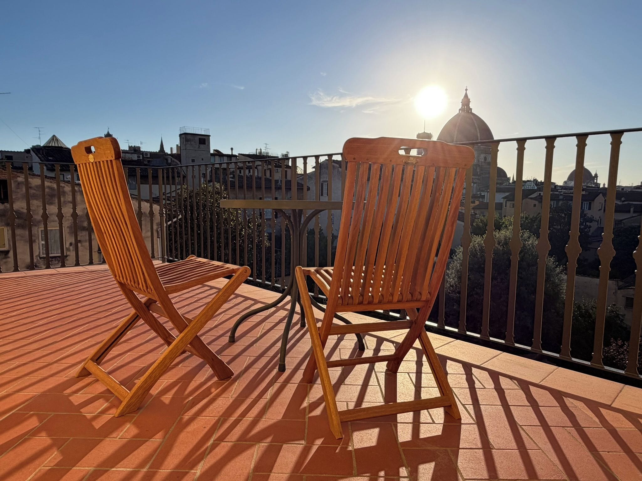 Two wooden chairs on a tiled balcony with a view of a cityscape and a dome in the background.