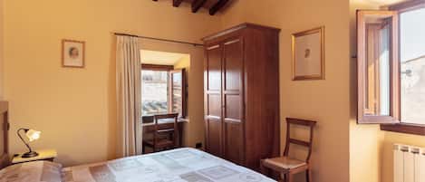 Une chambre à coucher comprenant un lit, une armoire en bois, une chaise, un bureau avec une lampe et une fenêtre avec des rideaux.