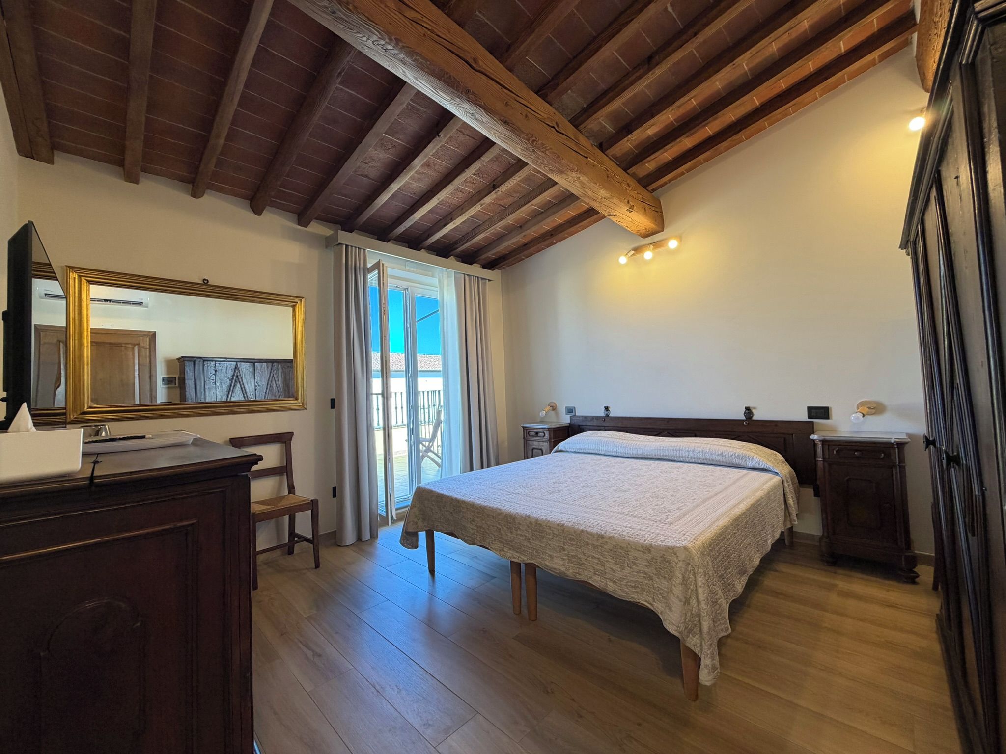 A bedroom with a wooden ceiling, a bed, a desk with a chair, and a large mirror.