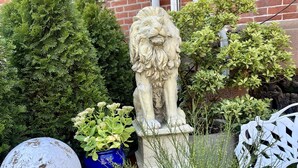 Un jardín con una estatua de león, un globo terráqueo y diversas plantas.