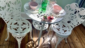 Una mesa redonda de vidrio con sillas blancas con motivos florales, sobre un piso de madera.