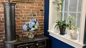 Una habitación con pared de ladrillo, estufa antigua, ventana con plantas y un cuadro en la pared.