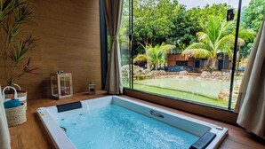 Zona de spa con hidromasaje, suelo de madera y vistas a una piscina y vegetación exterior.