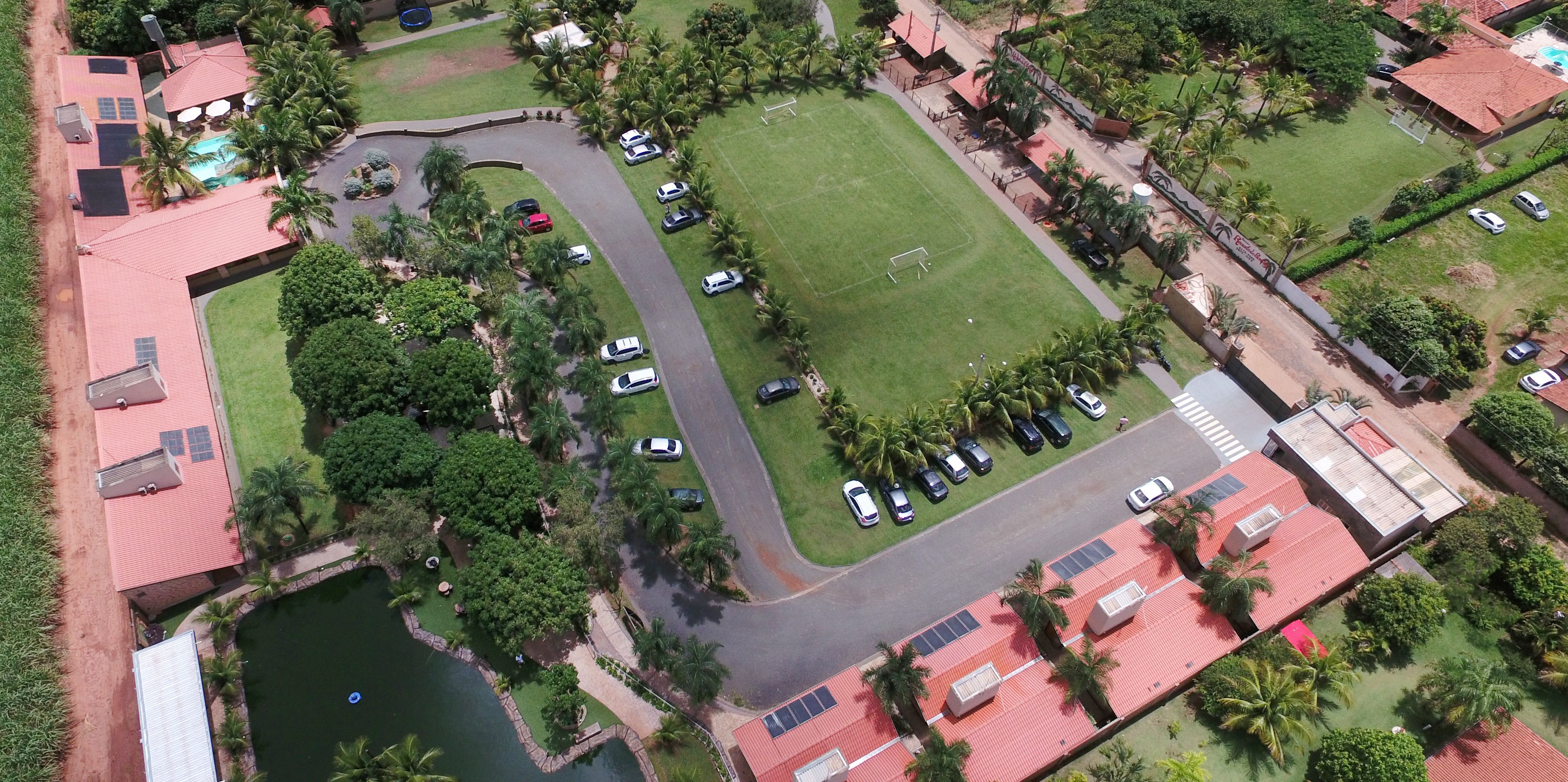 Vista aérea de uma área residencial com um grande campo verde, uma piscina e vários carros estacionados.