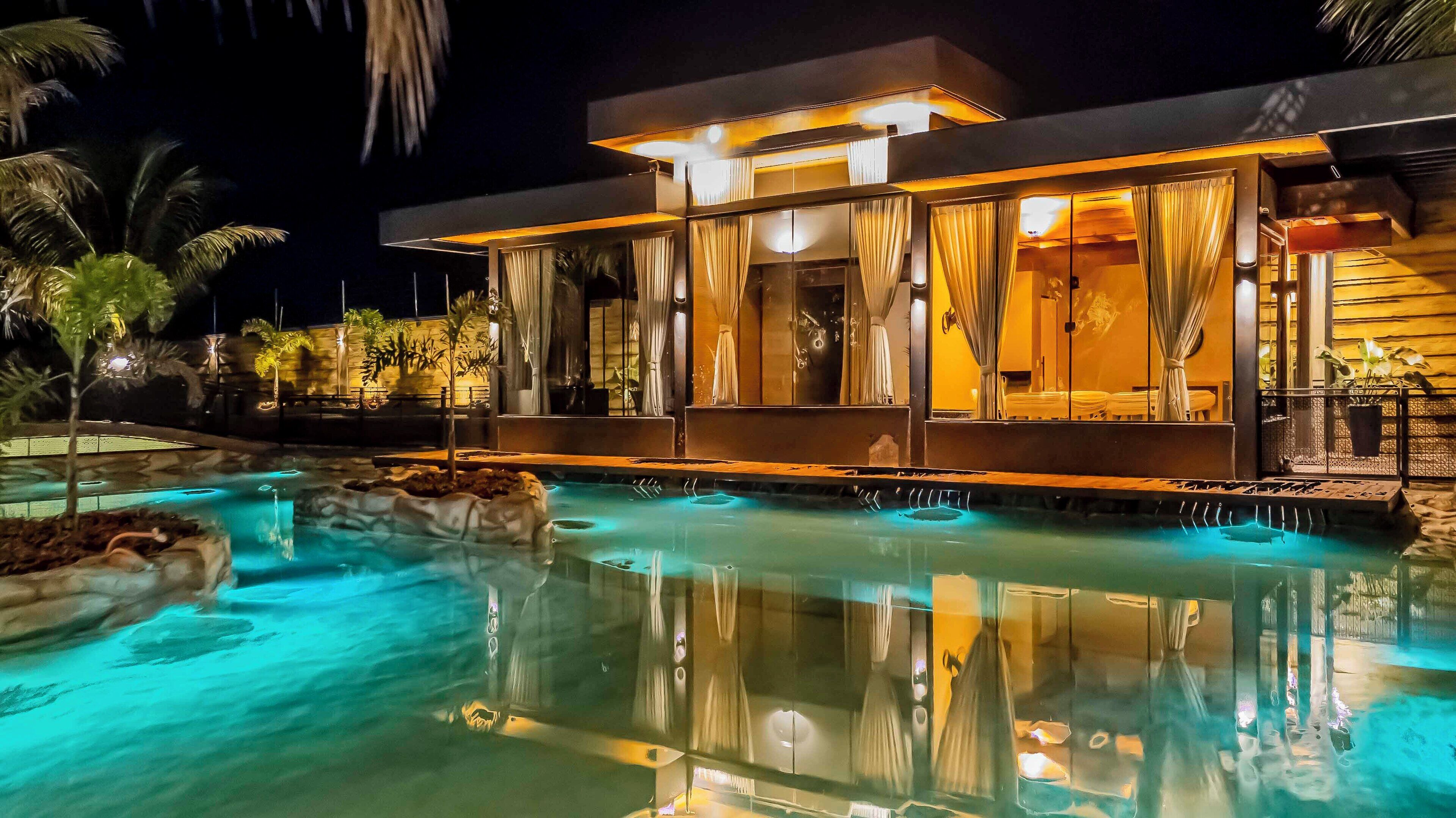 A modern hotel with a swimming pool, large windows, and tropical plants.