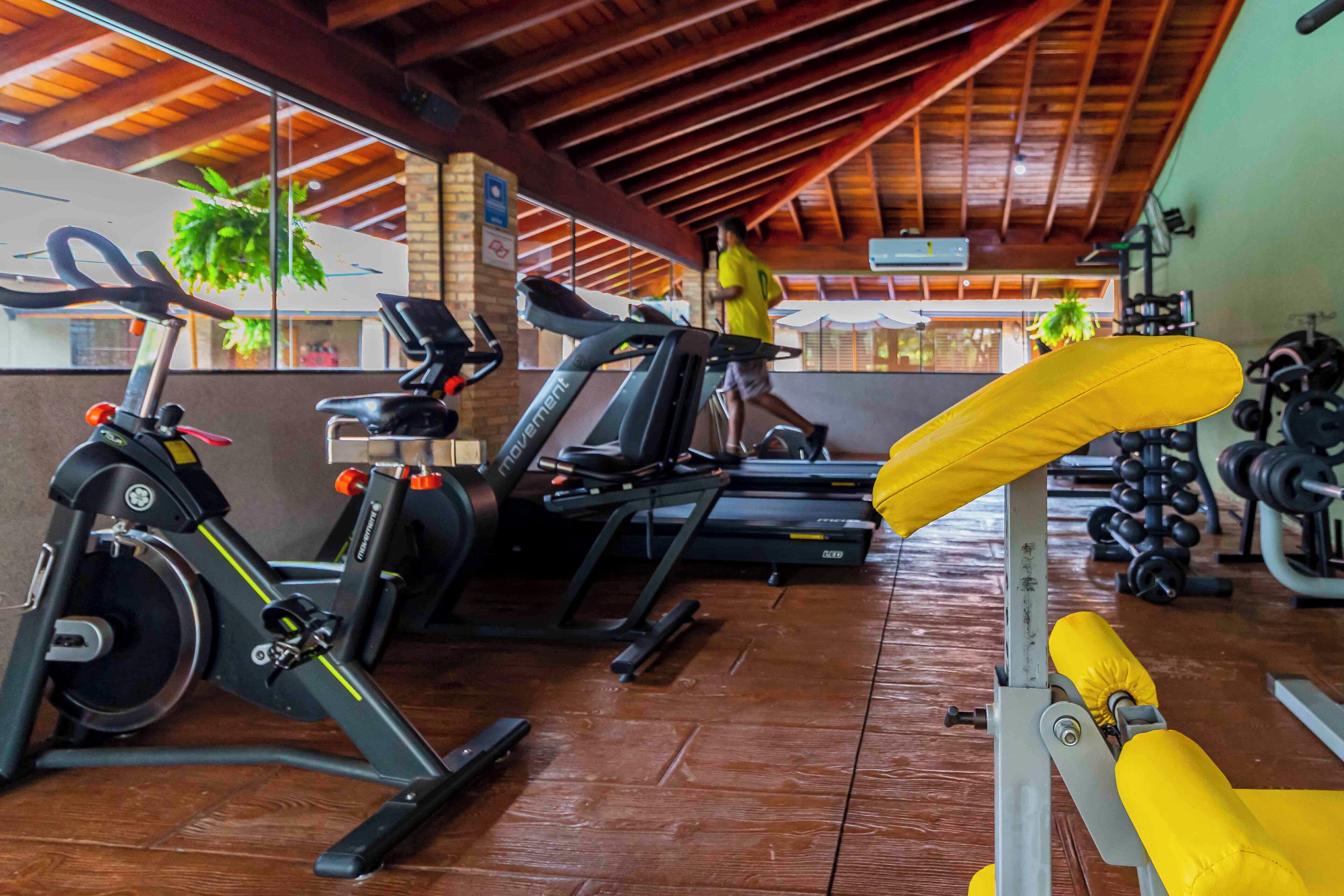 A gym with exercise equipment including treadmills and stationary bikes, wooden flooring, and a ceiling with exposed beams.