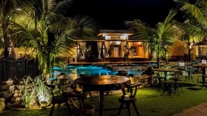 Un resort nocturno con piscina, zona de estar exterior y bar.