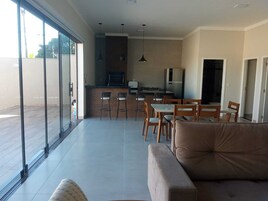Una cocina moderna con taburetes de bar, una mesa de comedor y un sofá en un amplio salón con ventanas grandes.