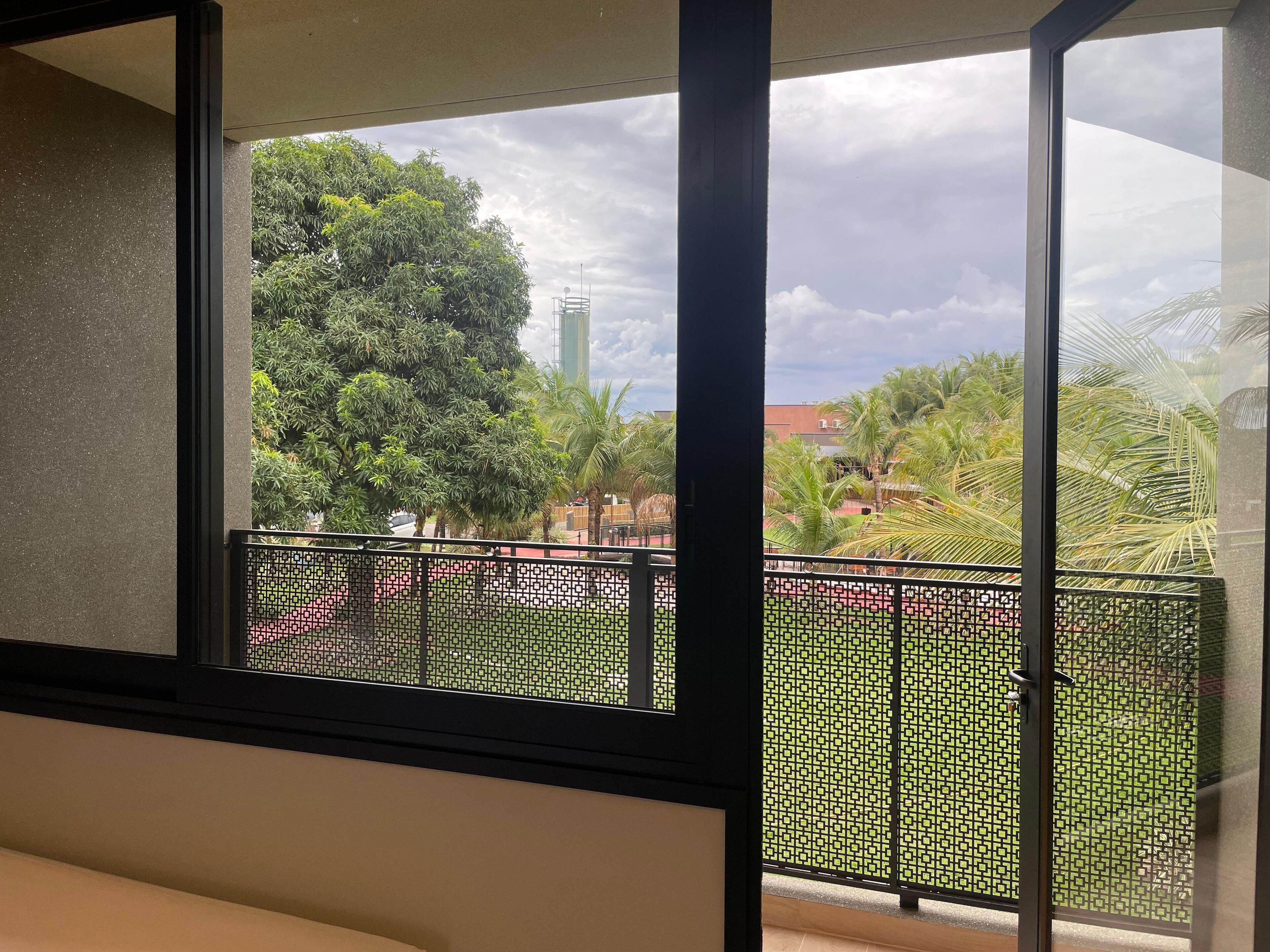 A balcony with a view of a green park and a tall building in the distance.