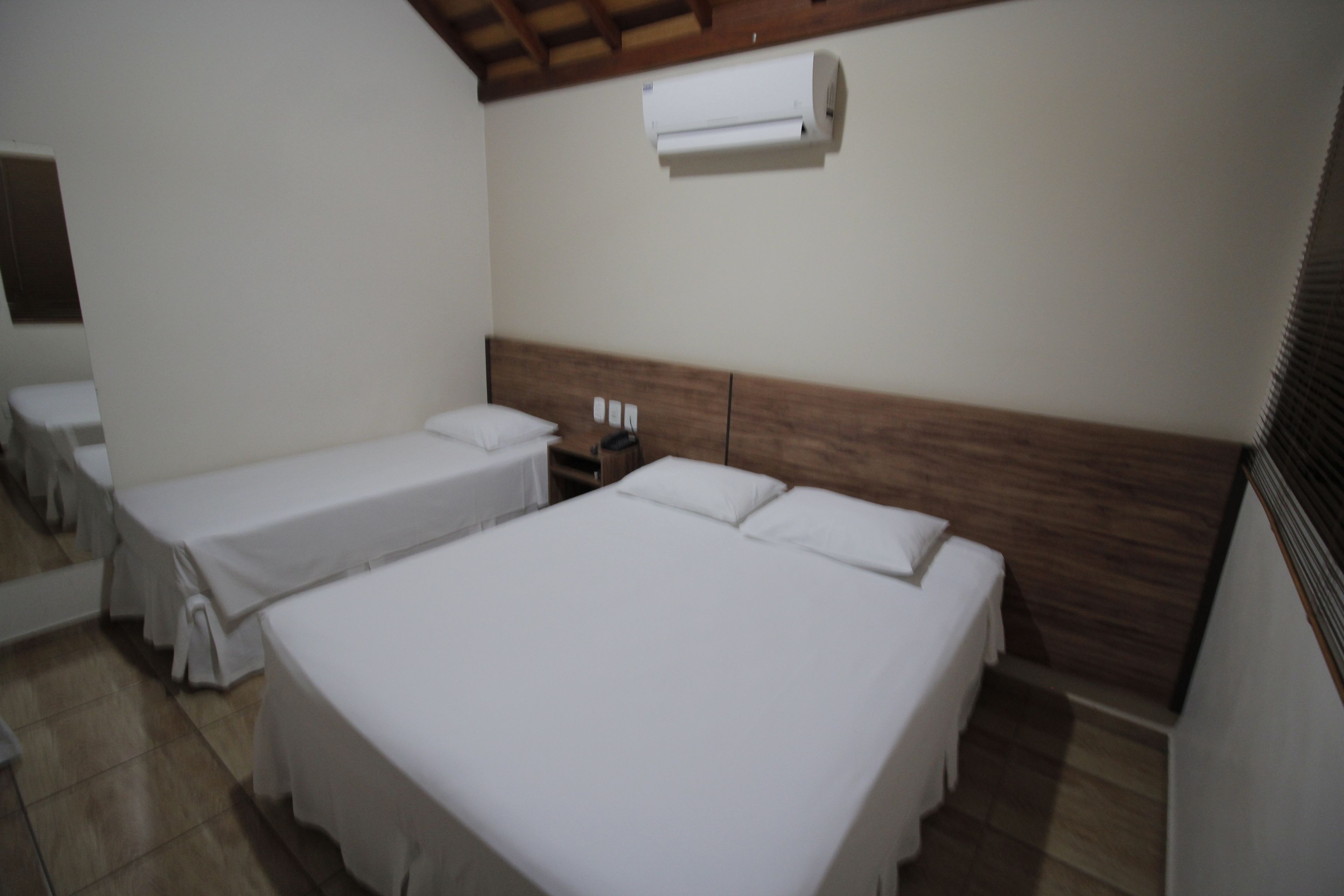 A hotel room with two single beds, a wooden headboard, a white air conditioner, and a tiled floor.