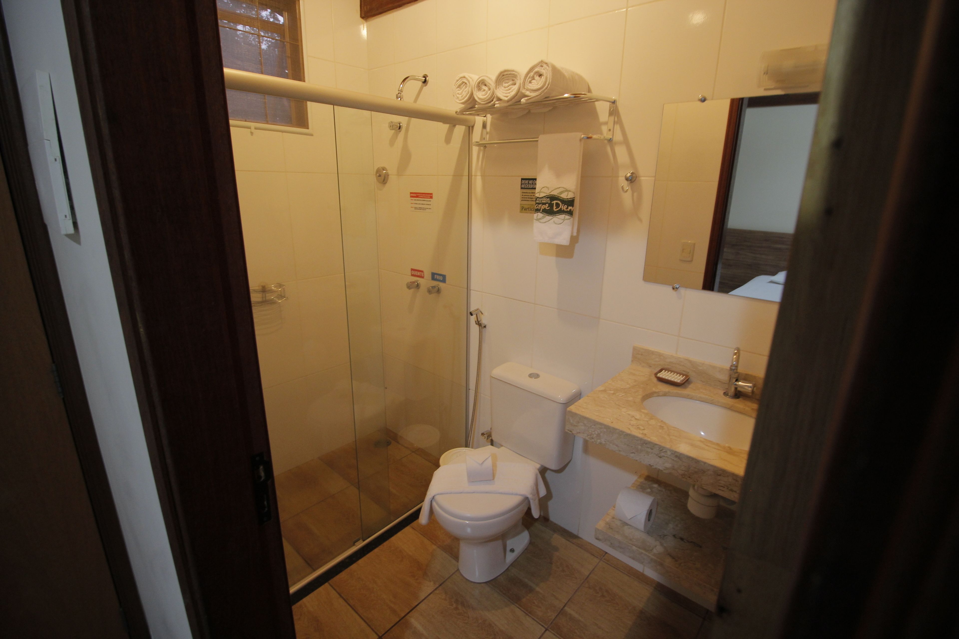 Un baño con cabina de ducha de vidrio, inodoro, lavabo con espejo y toallero con toallas.