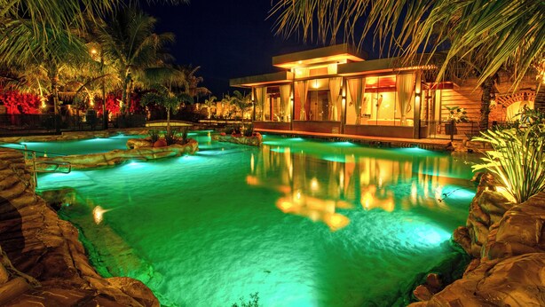 Un resort nocturno con piscina, palmeras y un edificio moderno.