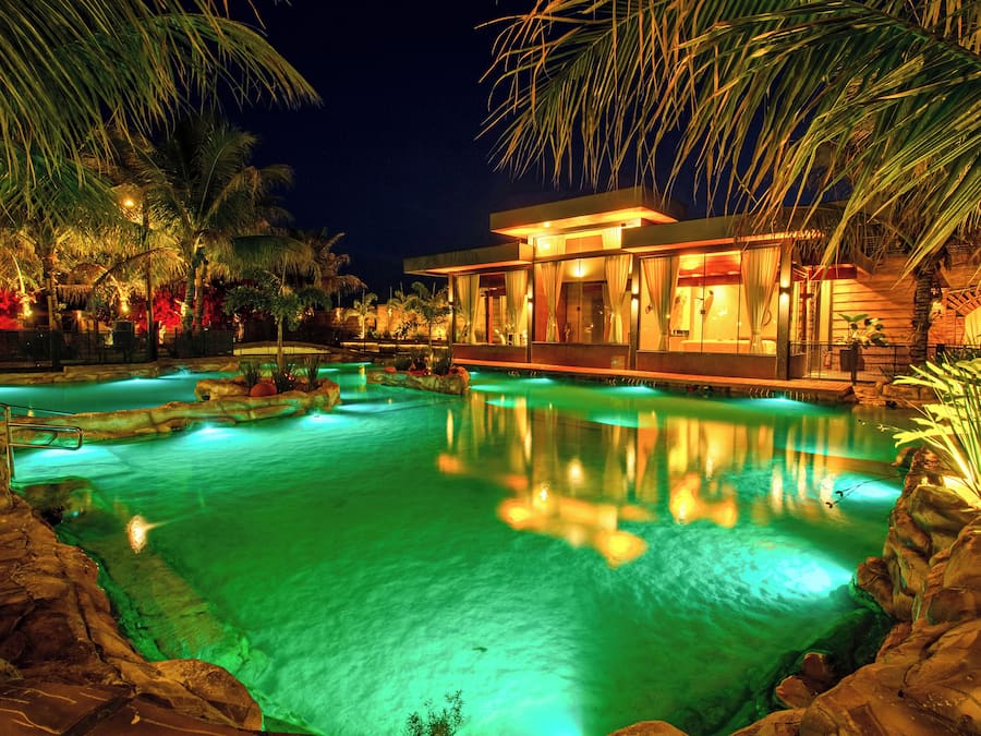 Un complexe hôtelier ouvert la nuit, doté d’une piscine, de palmiers et d’un bâtiment moderne.