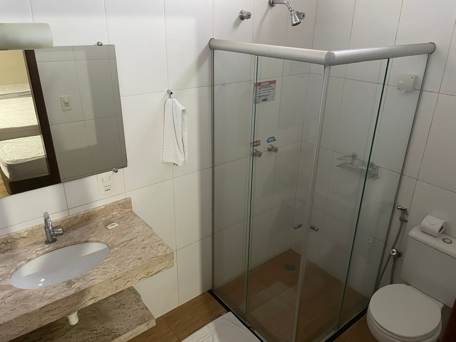 Un baño con ducha de vidrio, lavabo con encimera de mármol, inodoro y espejo.