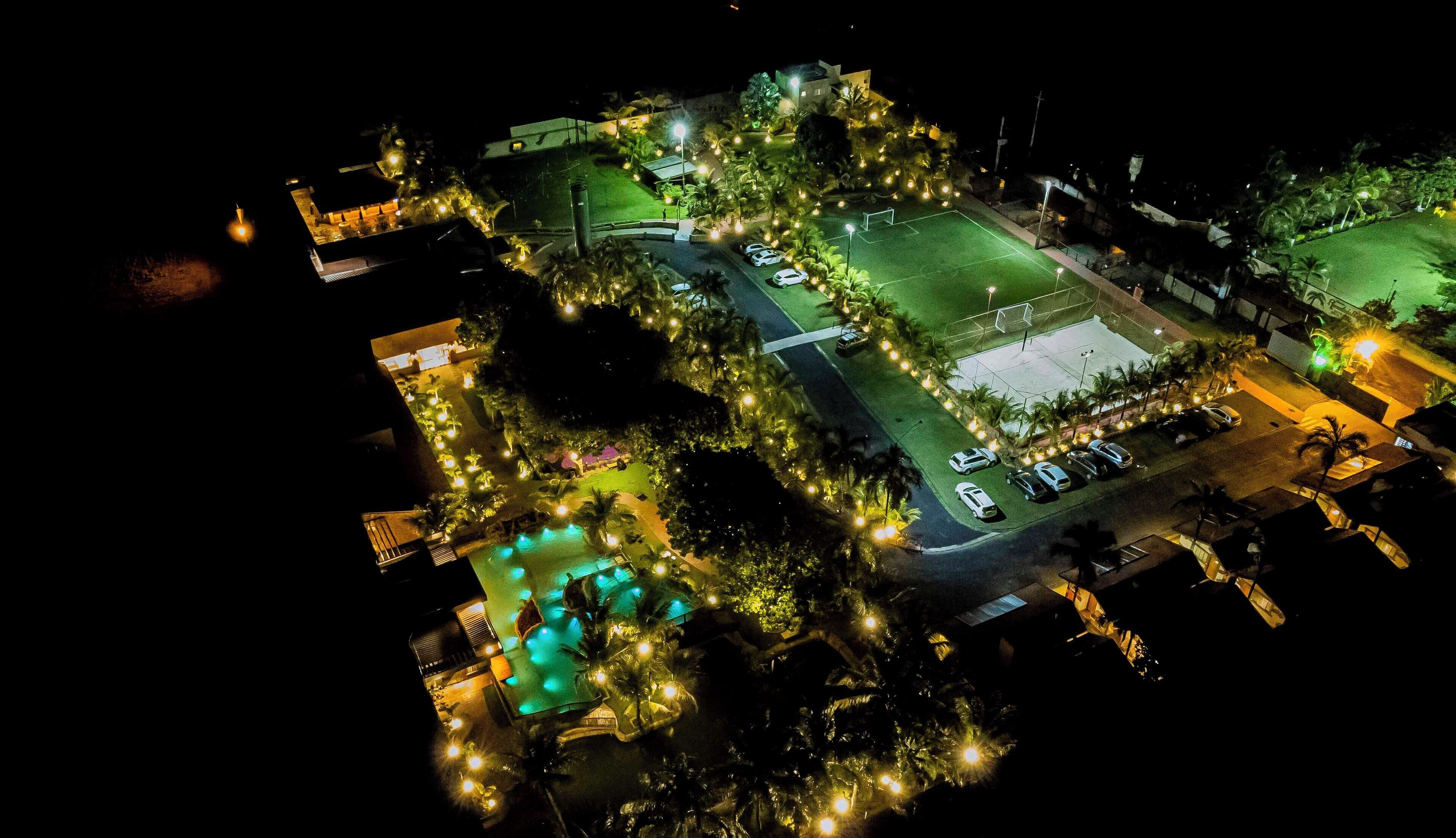 An aerial view of a resort with a swimming pool, a tennis court, and a parking area.