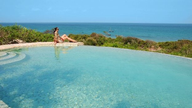 Ein klares, blaues Infinity-Pool mit einer Person, die am Rand entspannt und auf den Ozean blickt.