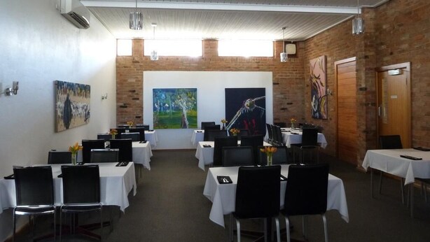 A conference room with tables set for a meeting, featuring a brick wall and artwork. - William Macintosh Motor Lodge (Naracoorte)