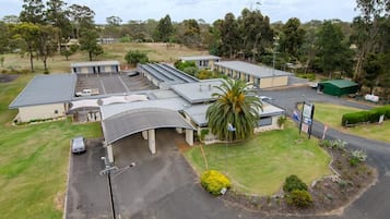 A building with multiple parking spaces, a covered parking area, and a green lawn with a palm tree.