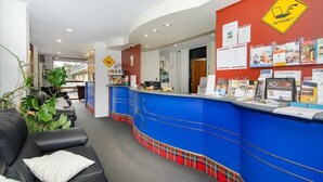 A reception area with a blue counter, a sign indicating internet availability, and a seating area with a couch and a plant. - William Macintosh Motor Lodge (Naracoorte)