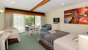 A hotel room with a bed, a desk, a chair, a television, and a large window with curtains. - William Macintosh Motor Lodge (Naracoorte)