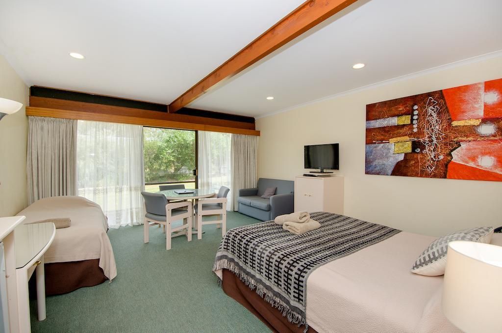A hotel room with a bed, a desk, a chair, a television, and a large window with curtains.