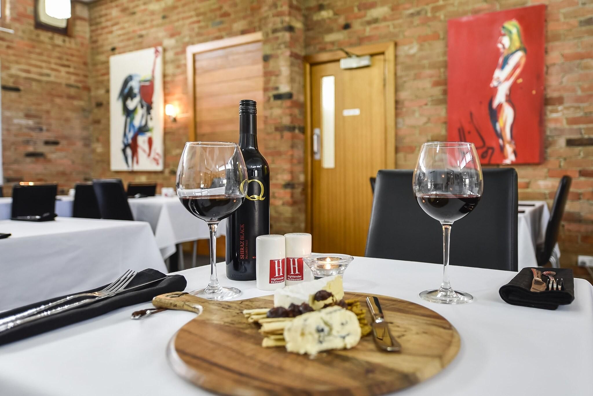 A dining table set with wine glasses, a bottle of wine, cheese, and crackers.