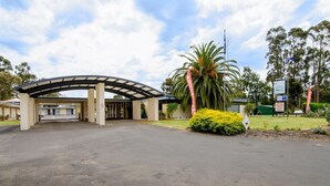 A hotel entrance with a covered driveway, palm trees, and a signboard. - William Macintosh Motor Lodge (Naracoorte)