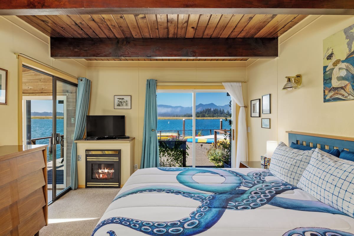 A bedroom with a large bed, a fireplace, a television, and a view of the sea.