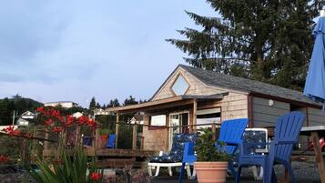 Ein Holzhaus mit geneigtem Dach, einer Sitzgelegenheit im Freien mit blauen Stühlen und einem Garten mit roten Blumen.