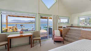 Una habitación con vista a un lago, un comedor con mesa y sillas, un sofá, una escalera y un baño con lavamanos y espejo.