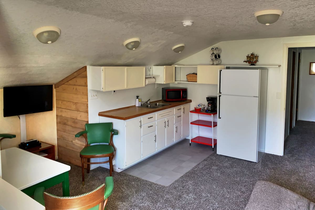 A compact kitchen with white cabinets, a microwave, a refrigerator, and a wooden dining table with chairs.