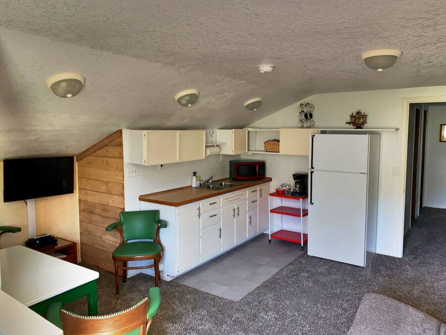 Eine kleine Küche mit weißen Schränken, einer Mikrowelle, einem Kühlschrank und einem Holzespeisetisch mit Stühlen.