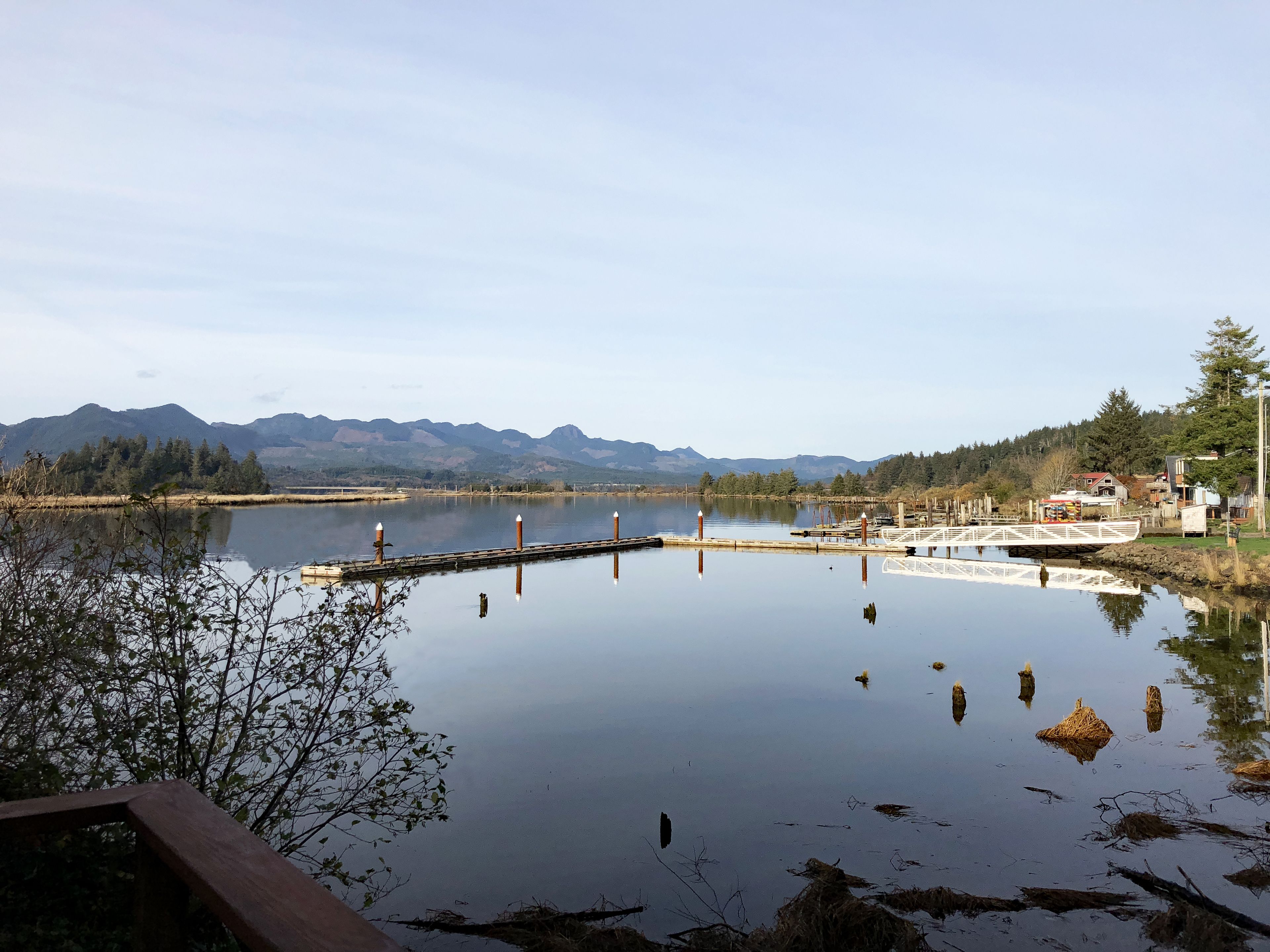 Um lago tranquilo com um cais e um pequeno edifício, cercado por montanhas e árvores.