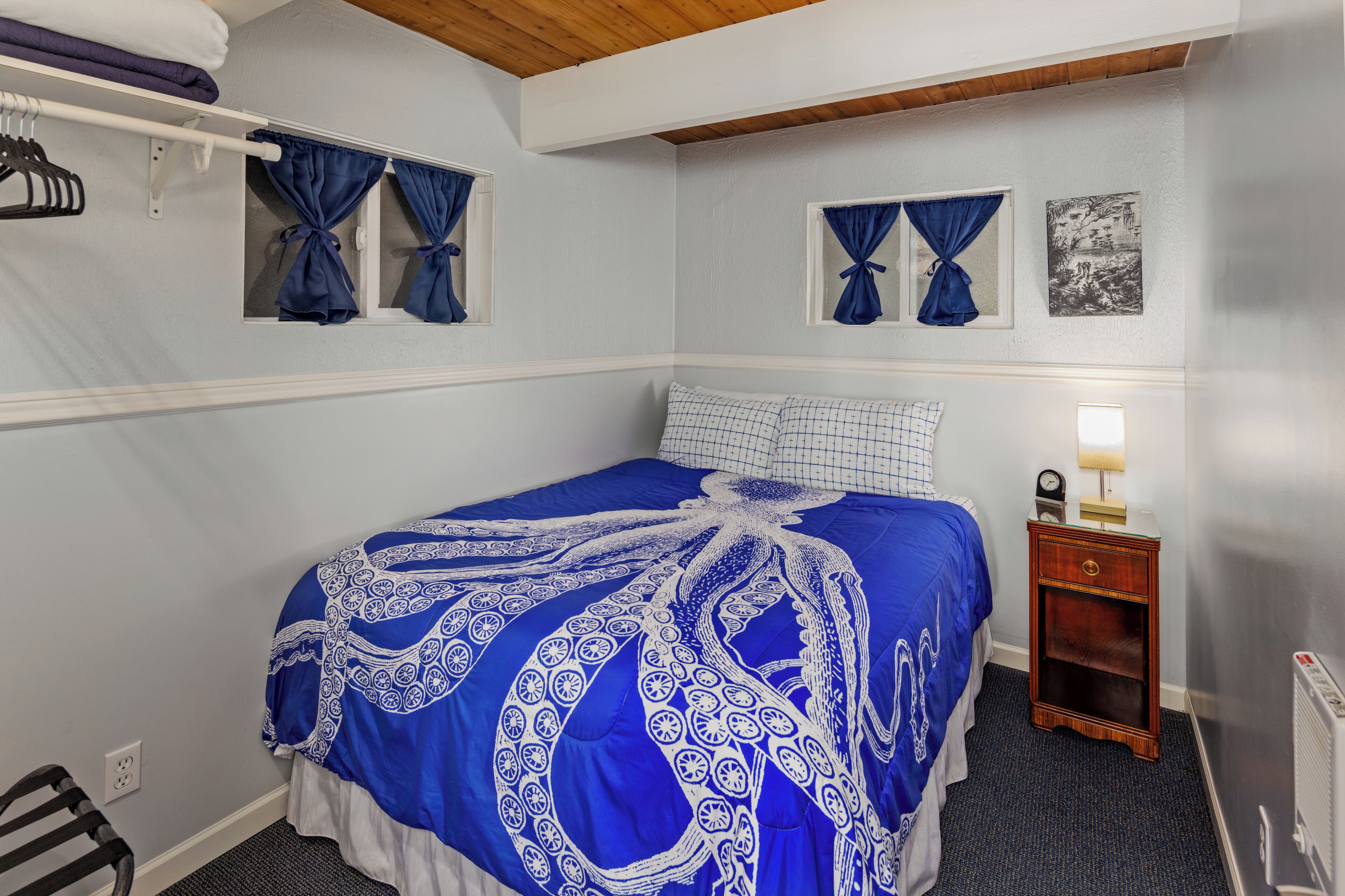 A bedroom with a bed, curtains, a nightstand, and a wall-mounted picture.
