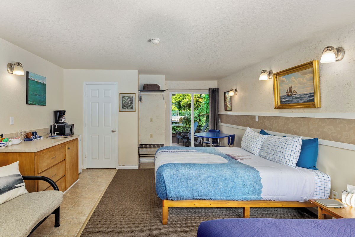 A bedroom with a bed, bedside table, and a view through a door to an outdoor area.