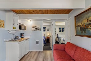 A compact living space with a kitchenette, a red sofa, and a painting of a harbor scene.
