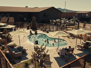 A pool area with lounge chairs and umbrellas, surrounded by buildings and a mountainous backdrop. - Red Roof Inn PLUS+ Williams - Grand Canyon (Williams)