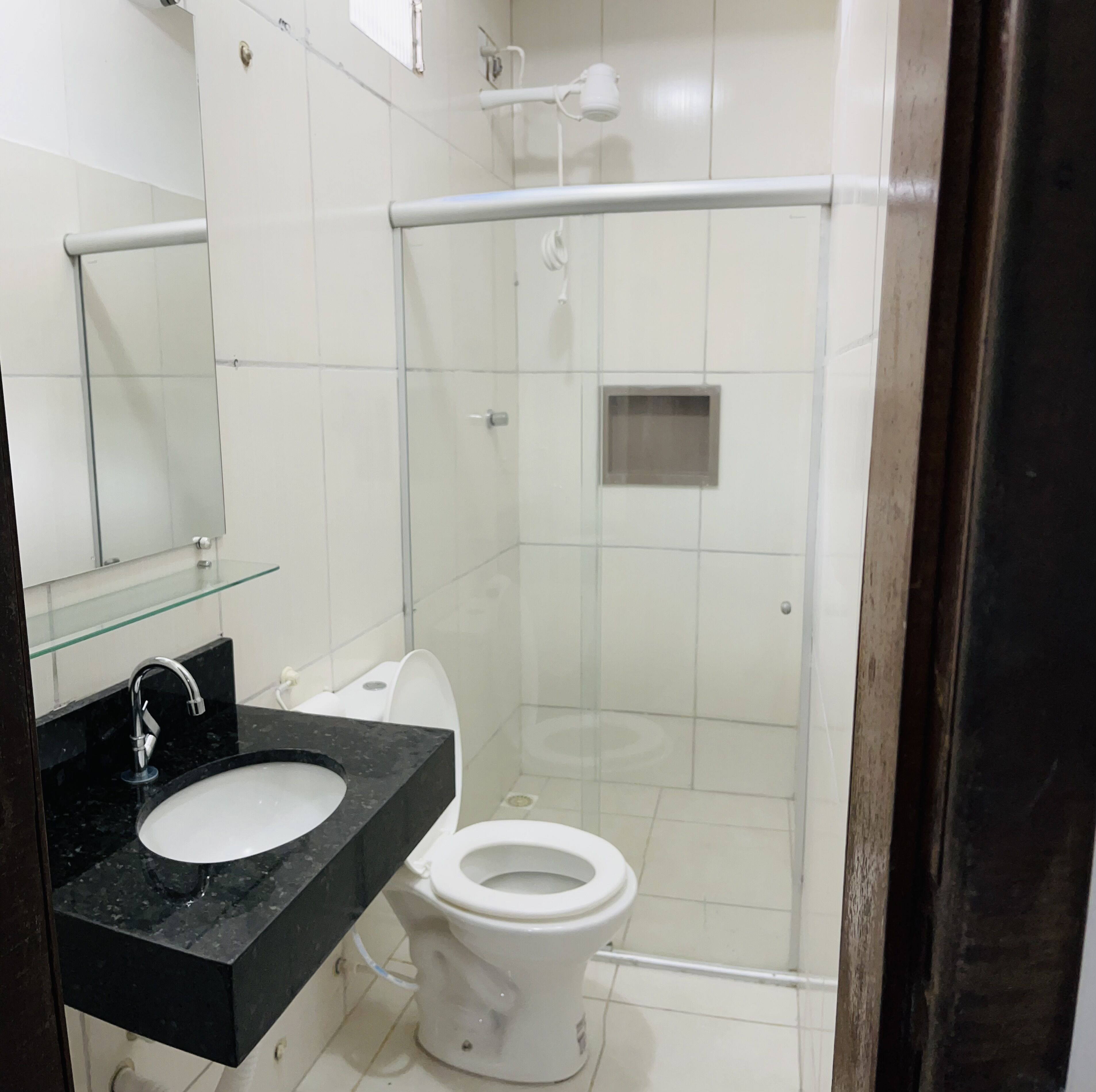 A modern bathroom with a glass shower enclosure, a white toilet, and a black marble sink.