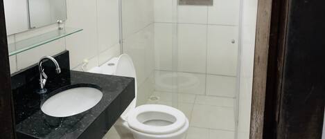 A modern bathroom with a glass shower enclosure, a white toilet, and a black marble sink.