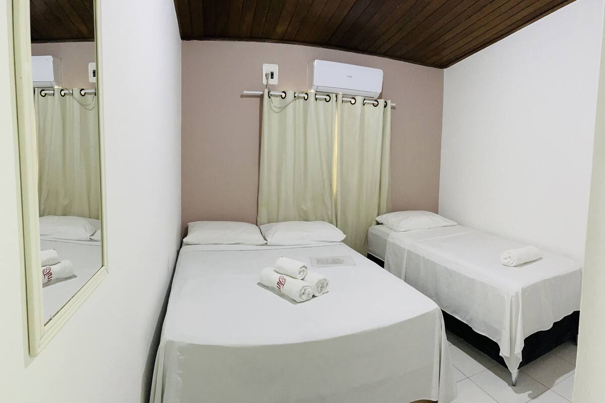 A hotel room with two single beds, a large mirror, a ceiling fan, and a window with curtains.
