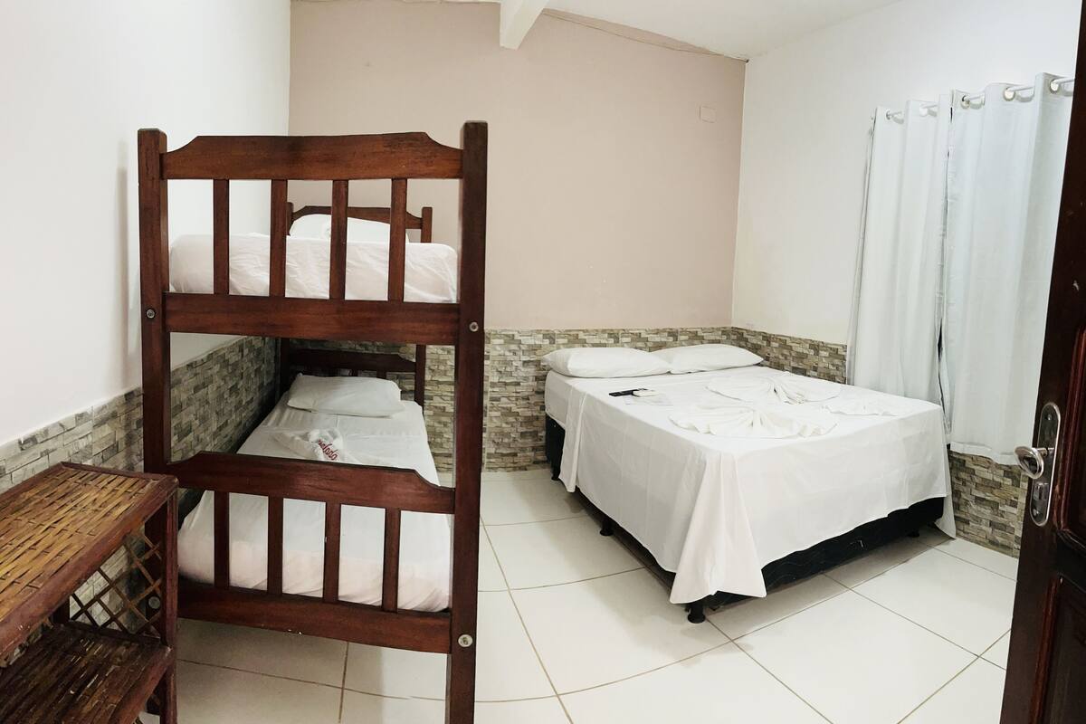 A room with a bunk bed, a single bed, a wooden table, and a tiled floor.